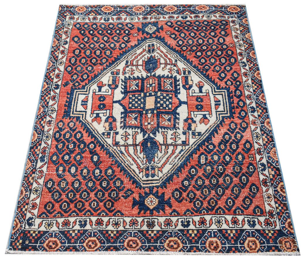 A handwoven vintage Persian rug featuring a central diamond medallion on a red and blue field.