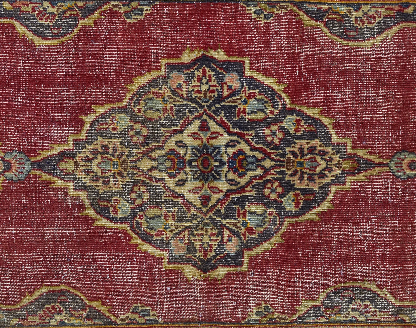 A vintage Persian rug featuring a central floral medallion in dark tones on a red field.
