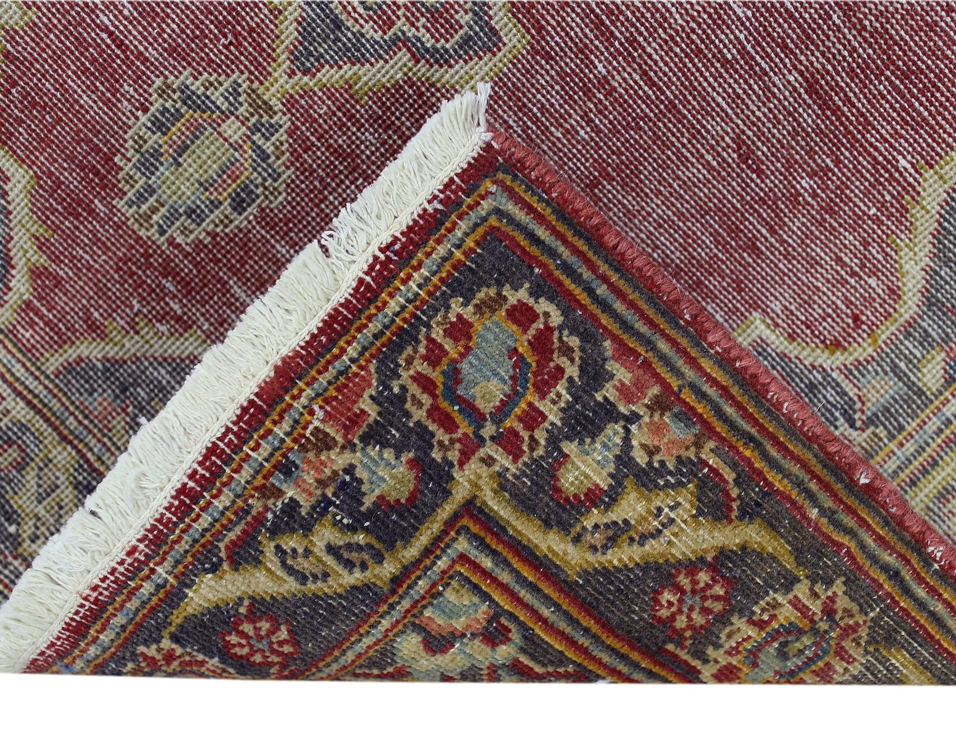 A corner of a vintage Persian rug with a red field and intricate floral patterns in wool.