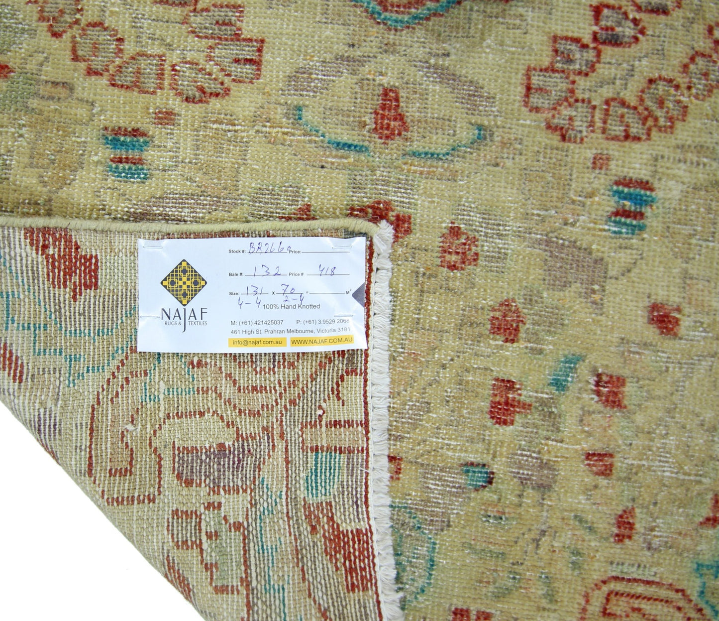 A vintage Persian rug with a faded floral pattern in red and green on a beige background.