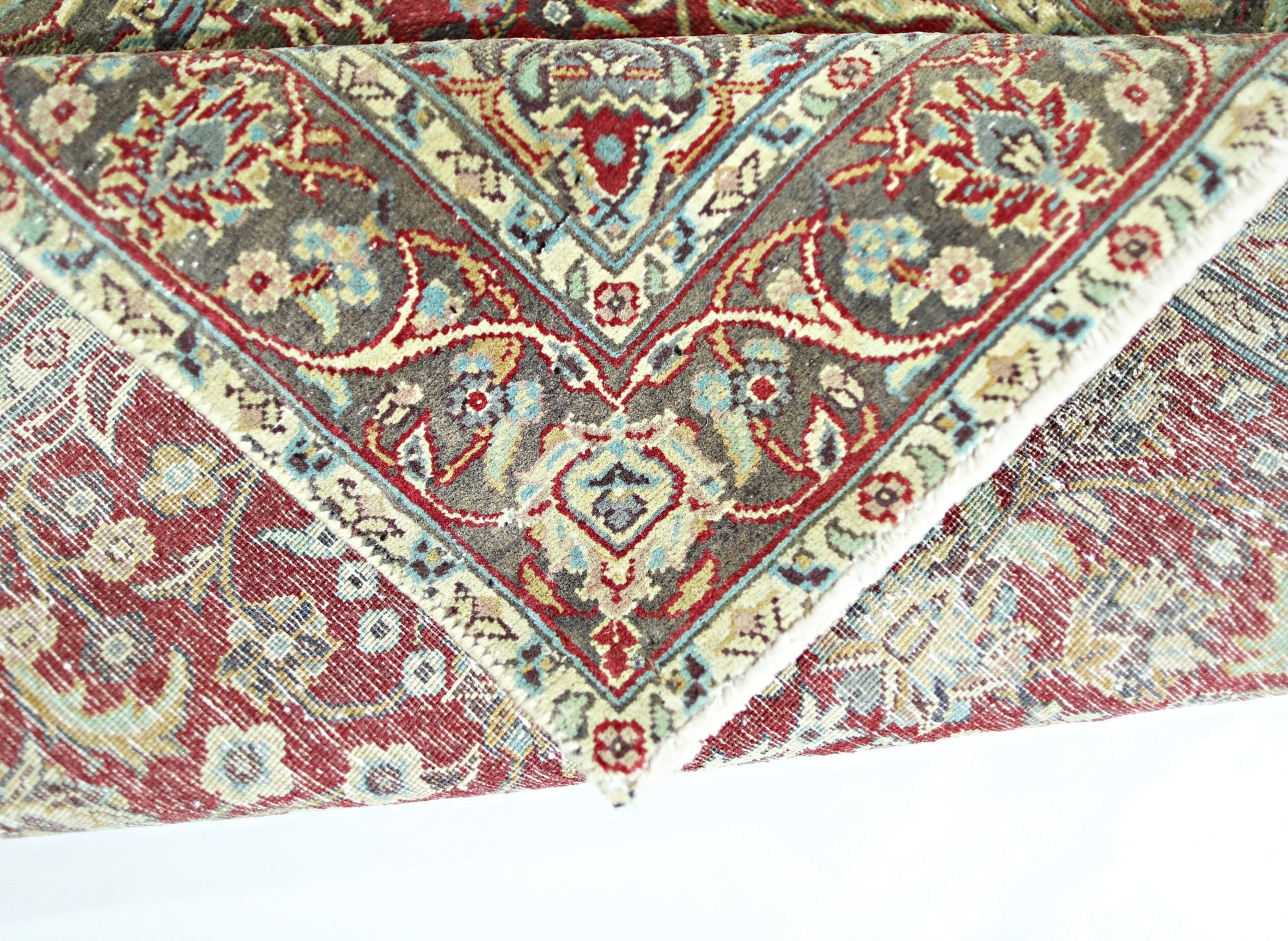 A folded vintage Persian rug featuring intricate floral patterns in red, blue, and beige tones.