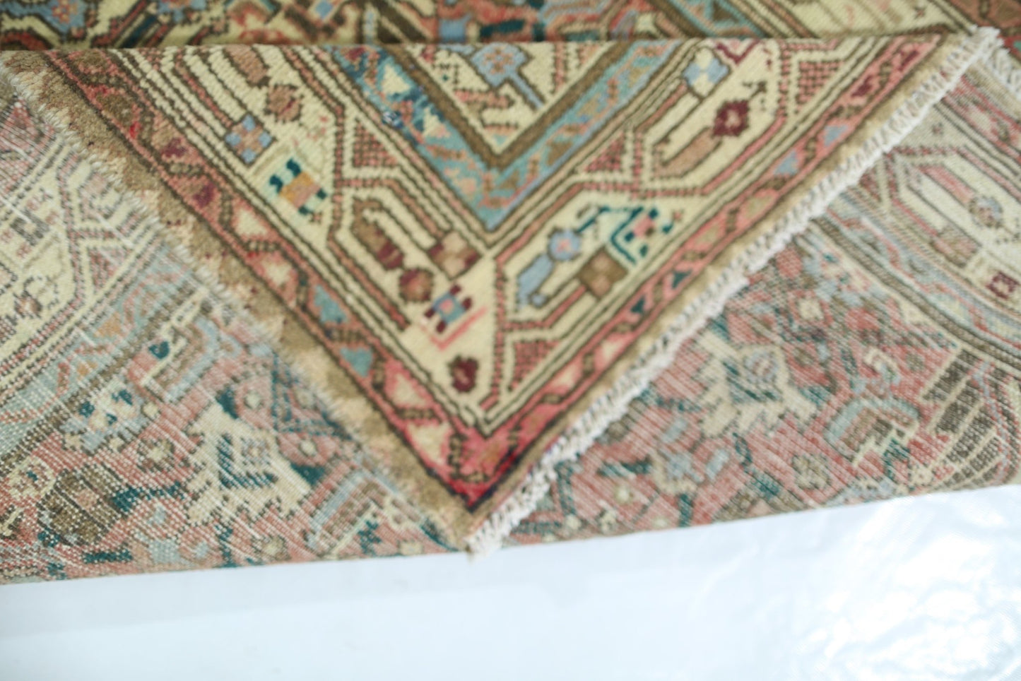A folded vintage Persian rug featuring intricate geometric patterns in muted red and blue tones.