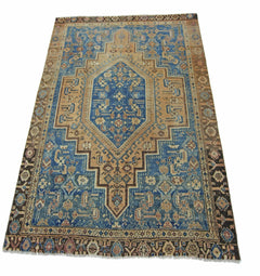 A vintage handmade Persian rug featuring a blue and tan geometric medallion pattern.