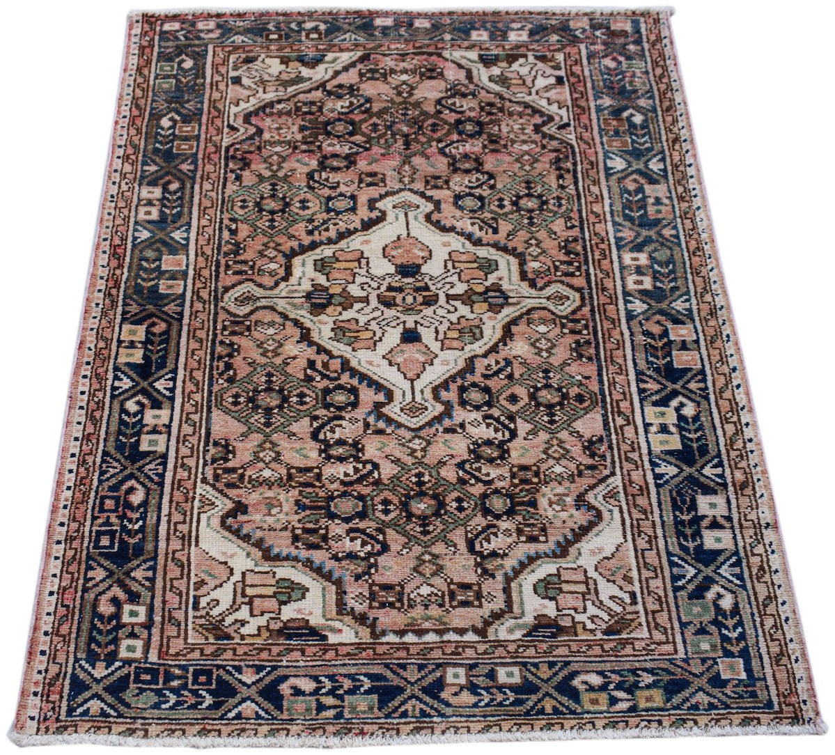 A vintage handwoven Persian rug featuring a central medallion on a pink field with blue borders.