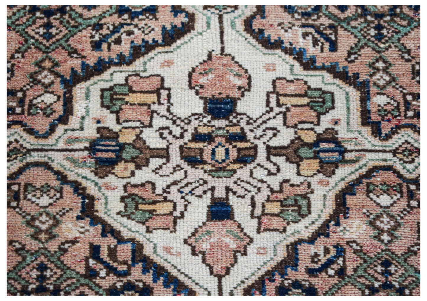 A vintage handwoven Persian rug featuring a central floral medallion in muted pink, blue, and cream.