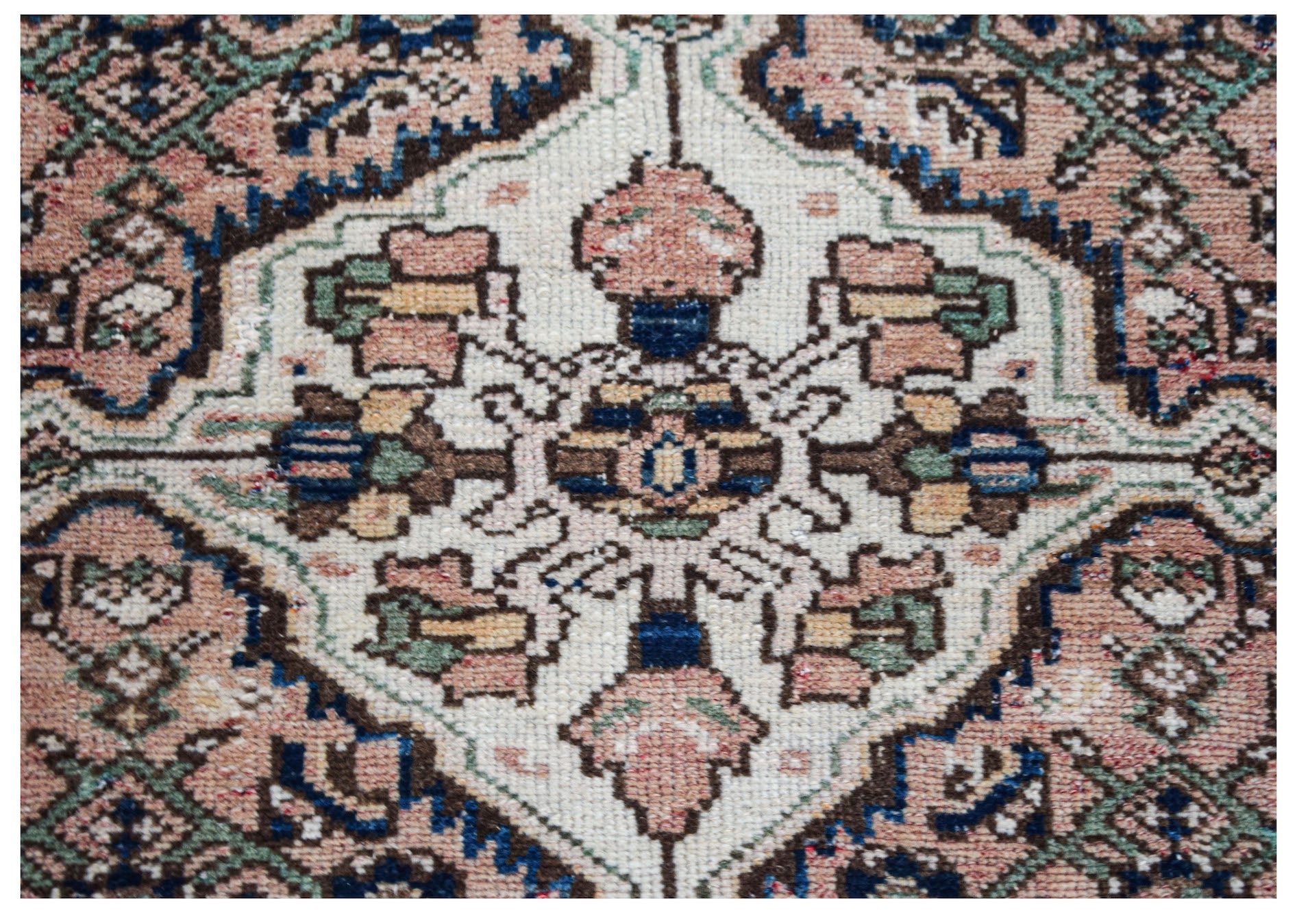 A vintage handwoven Persian rug featuring a central floral medallion in muted pink, blue, and cream.