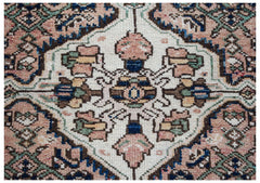 A vintage handwoven Persian rug featuring a central floral medallion in muted pink, blue, and cream.