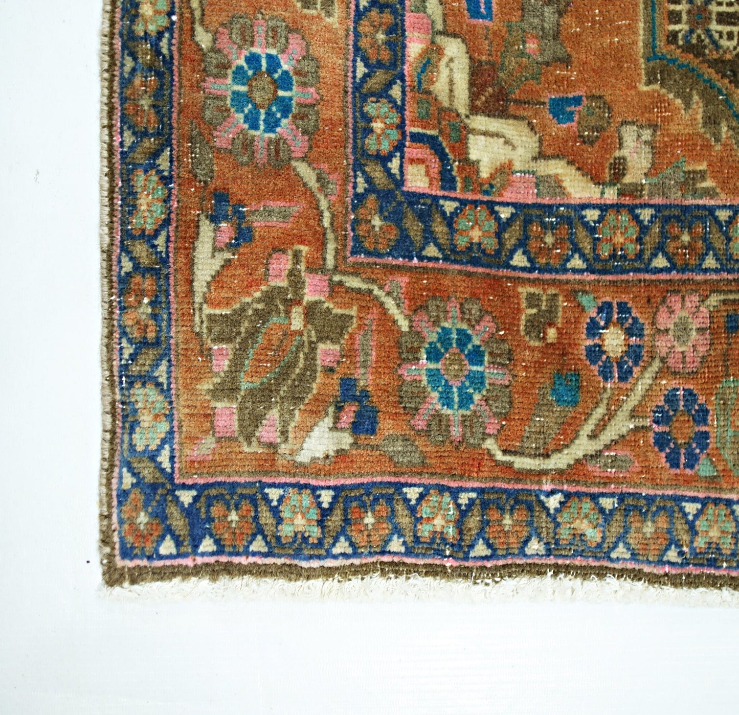 A vintage handmade Persian rug featuring a floral pattern in orange, blue, and pink tones.