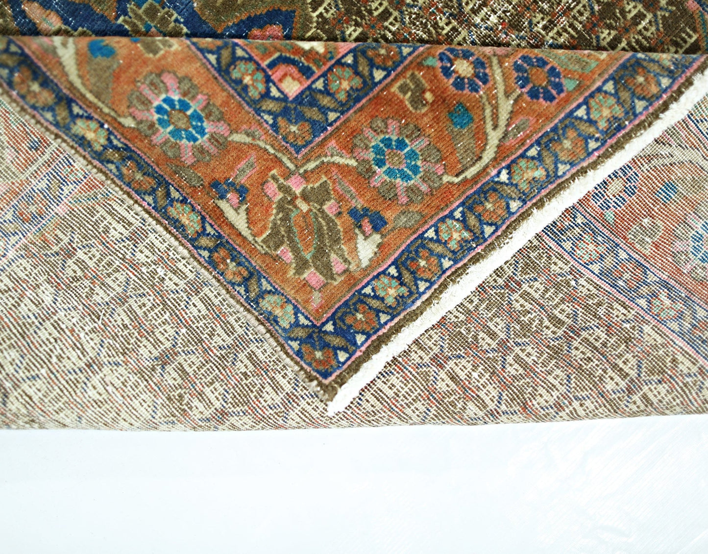 A folded vintage Persian rug featuring a floral pattern in orange, blue, and pink wool.