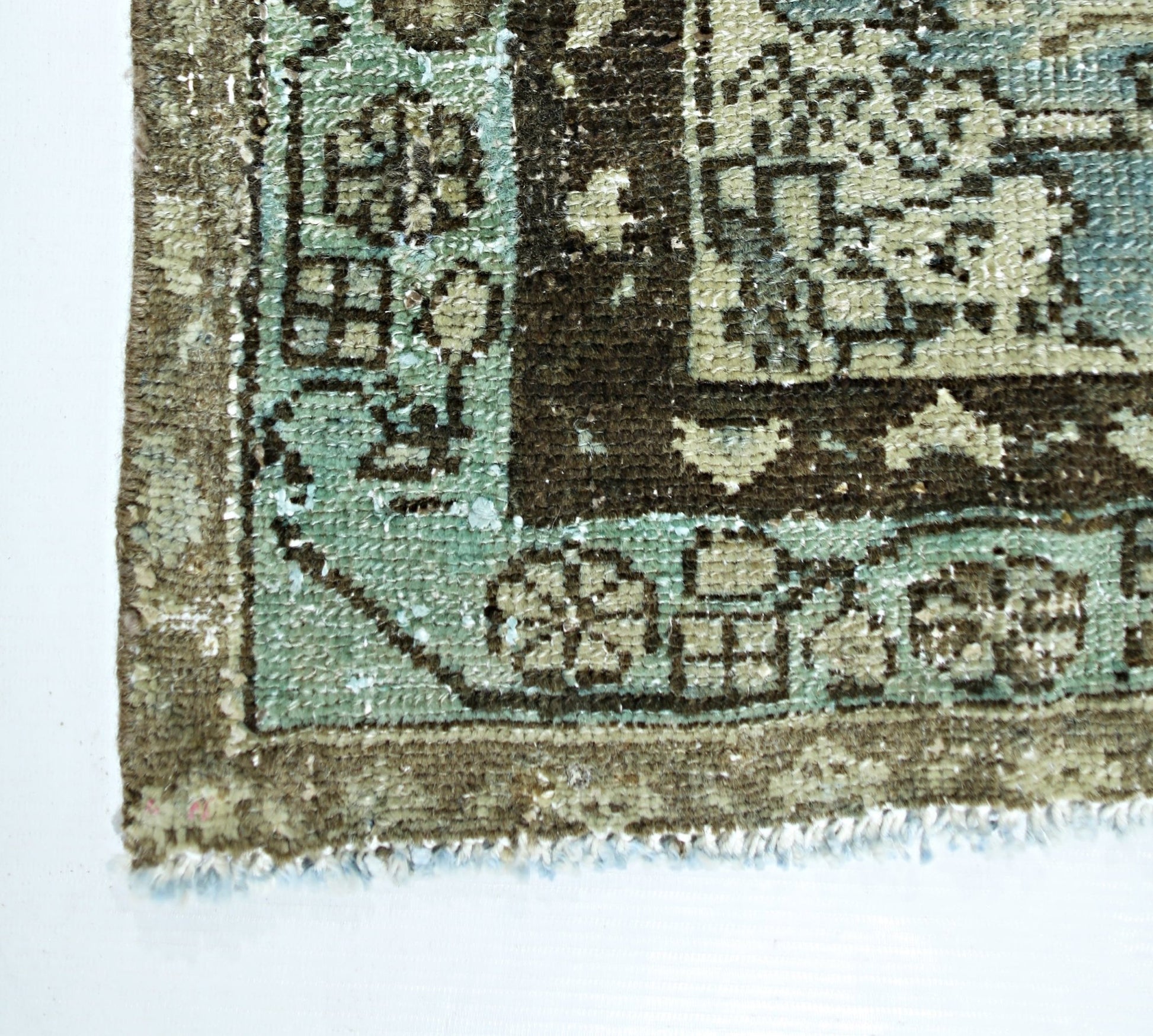 A corner view of a vintage handmade Persian rug featuring a floral pattern in teal and brown.
