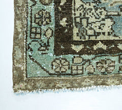 A corner view of a vintage handmade Persian rug featuring a floral pattern in teal and brown.