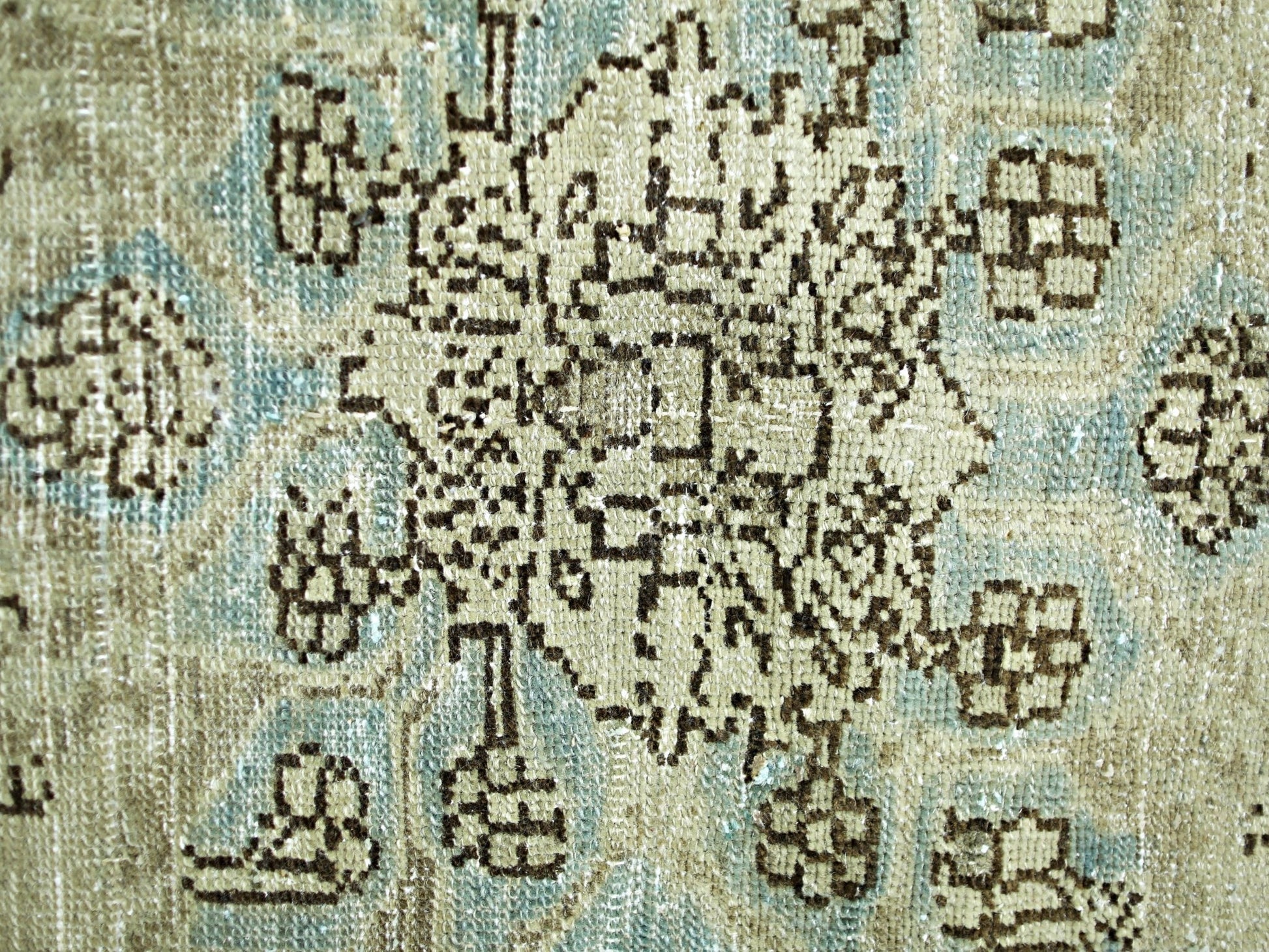 A close-up of a vintage Persian rug featuring a geometric floral pattern in blue and beige.