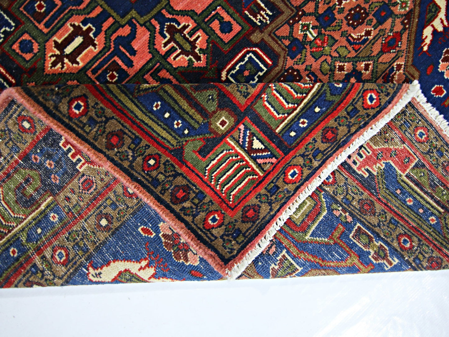 A vintage handmade Persian rug featuring intricate geometric patterns in red, blue, and green.