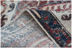 A handwoven vintage Persian rug with a worn texture and traditional red and blue floral patterns.
