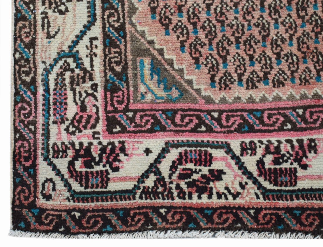 A handwoven vintage Persian rug featuring a pink central field with paisley patterns and borders.