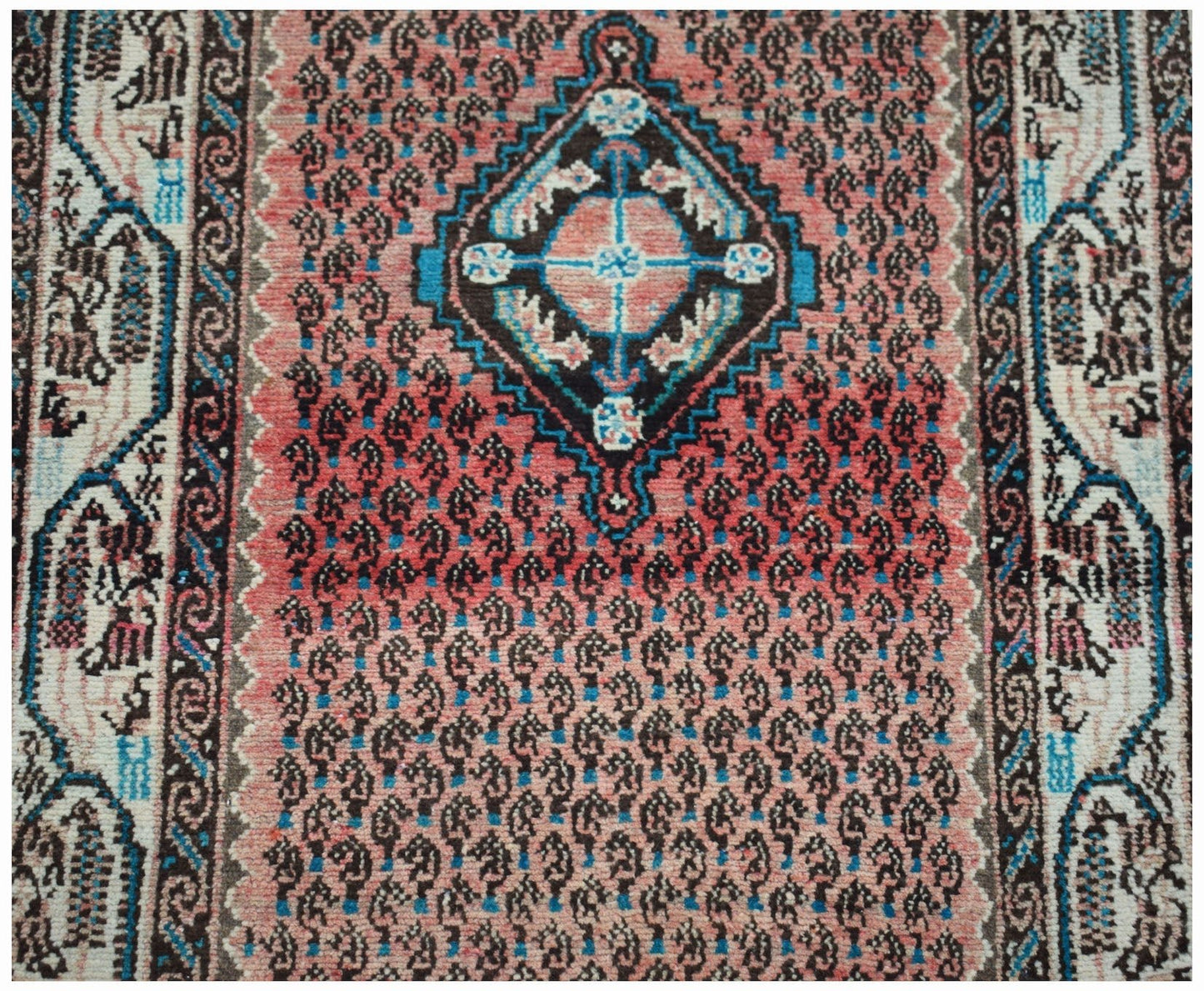 A vintage handwoven Persian rug featuring a central diamond medallion on a pink paisley field.