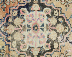 A vintage Persian rug featuring a central floral medallion in pink, blue, and cream on a dark field.