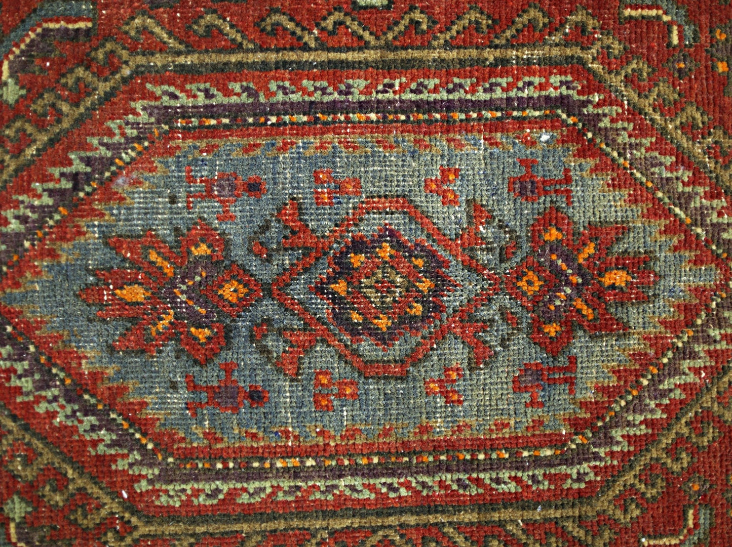A vintage Persian rug featuring a central geometric medallion in blue, red, and orange tones.