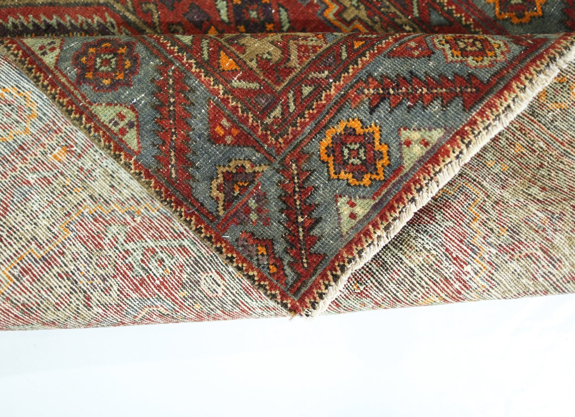 A folded vintage Persian rug featuring intricate geometric patterns in red, blue, and orange.