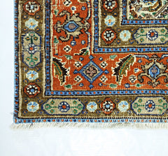 A vintage handmade Persian rug featuring intricate geometric patterns in orange, blue, and tan.