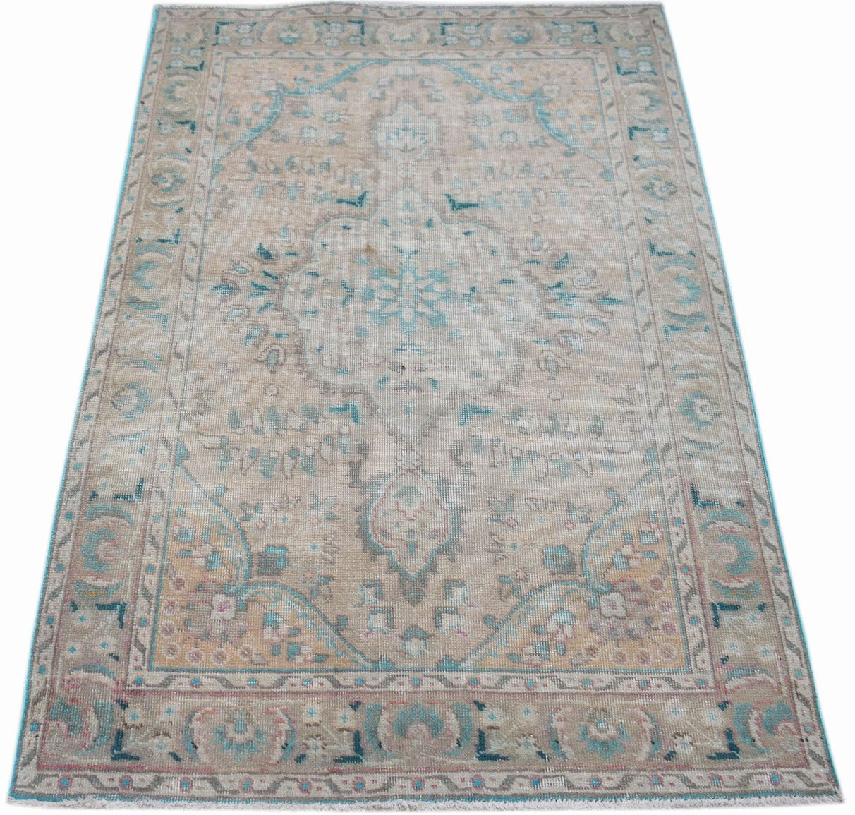 A vintage handwoven Persian rug featuring a faded floral medallion pattern in beige and teal.