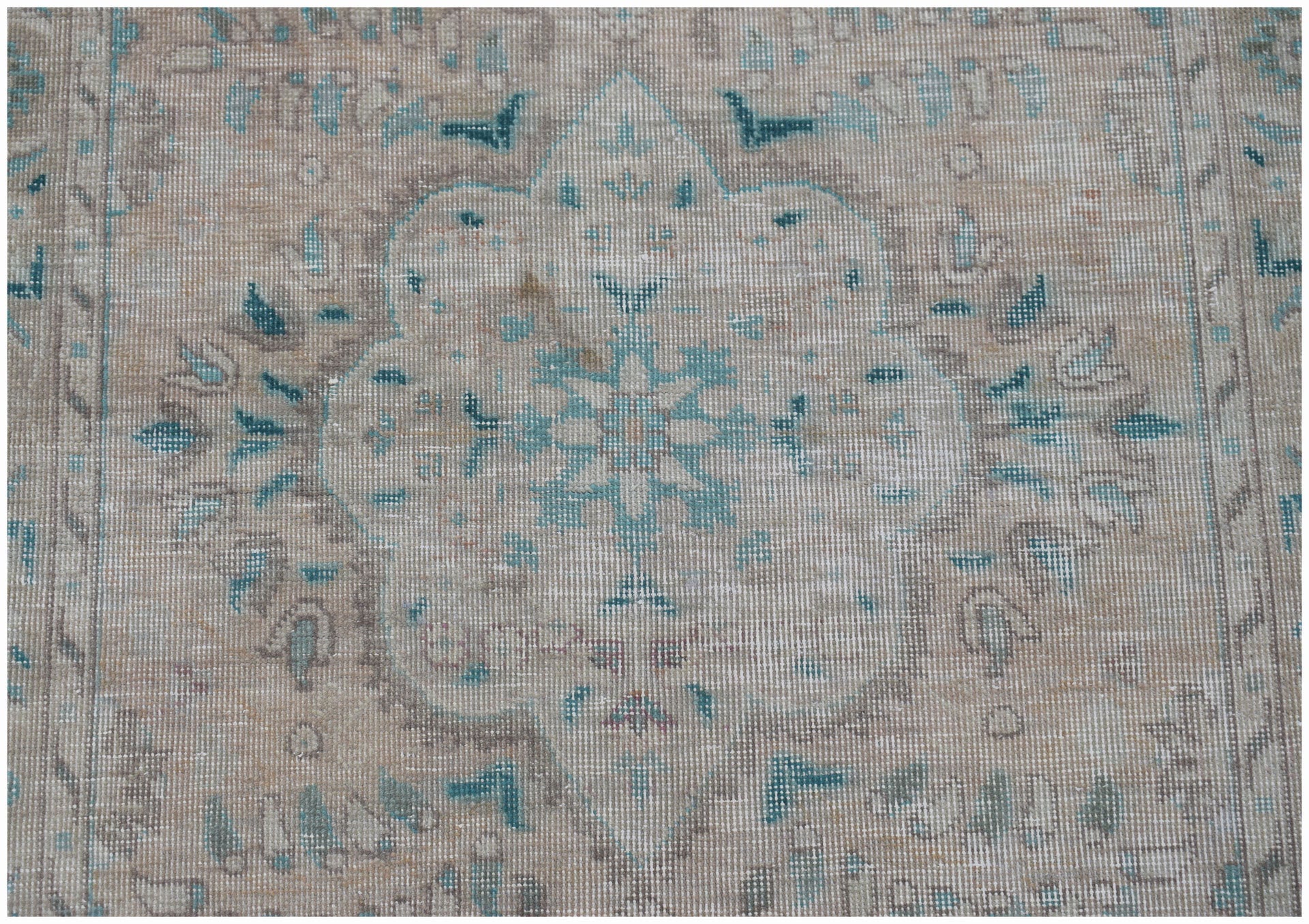 A vintage handwoven Persian rug featuring a faded floral medallion in blue and beige tones.