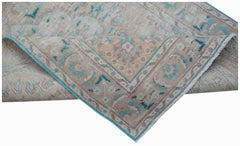 A handwoven vintage Persian rug featuring a faded floral pattern in beige, blue, and pink tones.