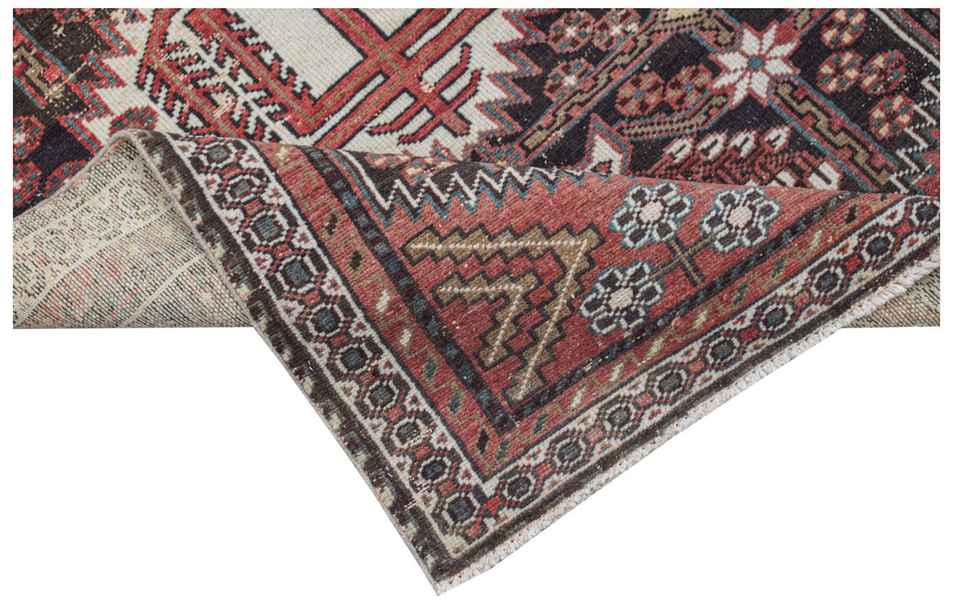 A handwoven vintage Persian rug featuring geometric patterns in red, black, and cream tones.