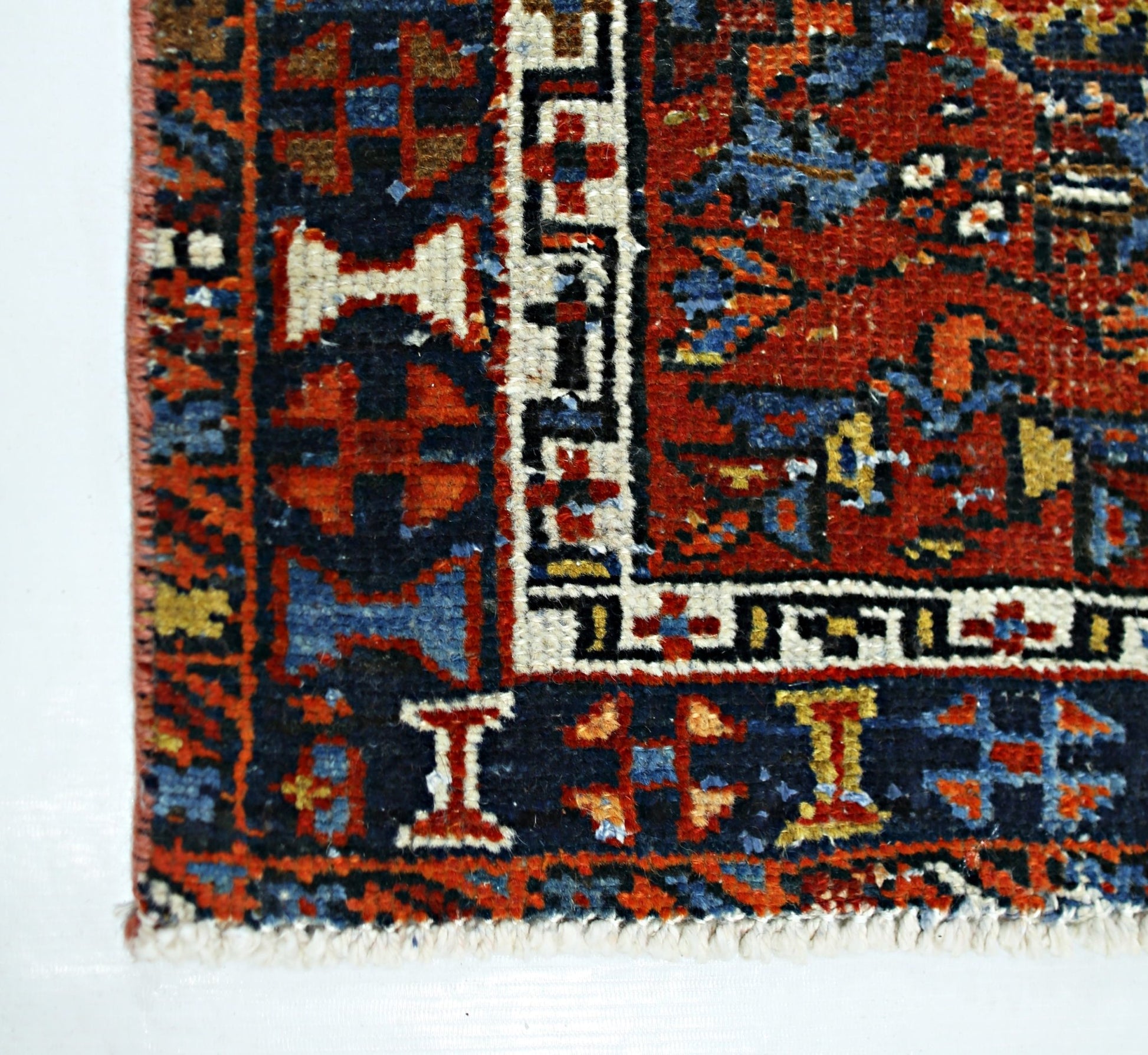 A close-up of a vintage handmade Persian rug featuring intricate geometric patterns in red and blue.