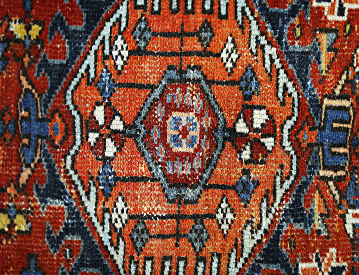 A close-up of a vintage Persian rug featuring a central orange medallion with intricate patterns.