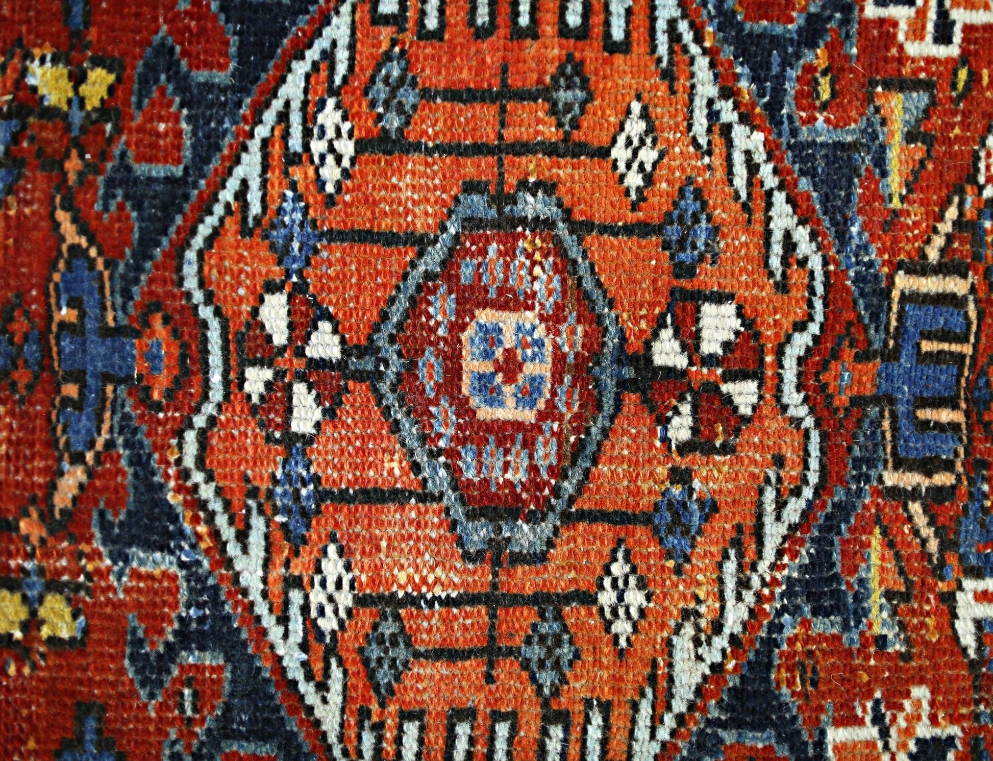 A close-up of a vintage Persian rug featuring a central orange medallion with intricate patterns.