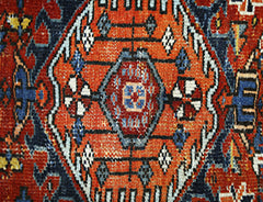 A close-up of a vintage Persian rug featuring a central orange medallion with intricate patterns.