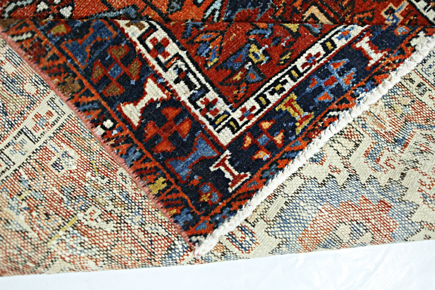 A folded vintage Persian rug featuring intricate geometric patterns in red, blue, and cream.