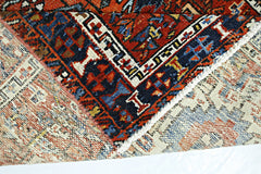 A folded vintage Persian rug featuring intricate geometric patterns in red, blue, and cream.