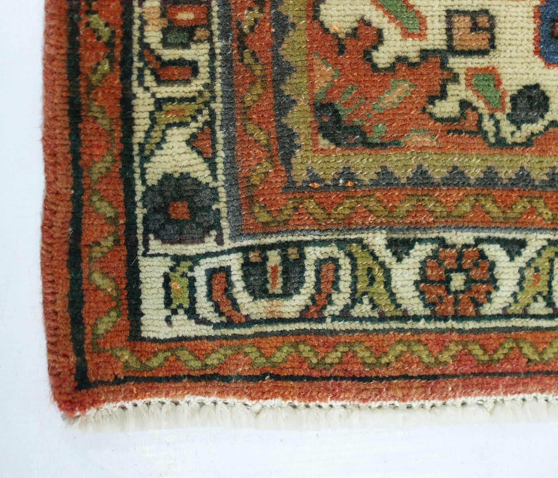 A close-up of a vintage handmade Persian rug featuring intricate geometric patterns in red, green, and cream.