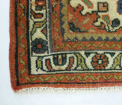 A close-up of a vintage handmade Persian rug featuring intricate geometric patterns in red, green, and cream.