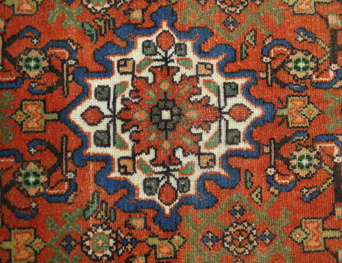 A vintage handmade Persian rug featuring a central geometric floral medallion in red, blue, and cream.
