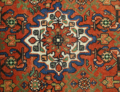 A vintage handmade Persian rug featuring a central geometric floral medallion in red, blue, and cream.