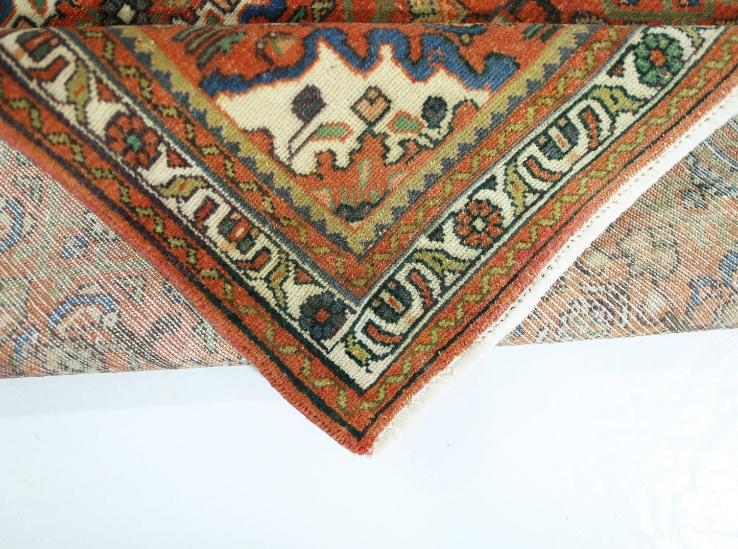 A corner of a vintage handmade Persian rug showing intricate geometric patterns in wool.