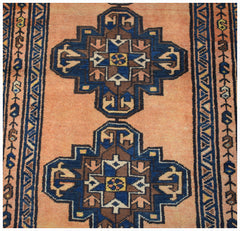 A vintage handwoven Persian rug featuring two blue and brown geometric medallions on a peach field.