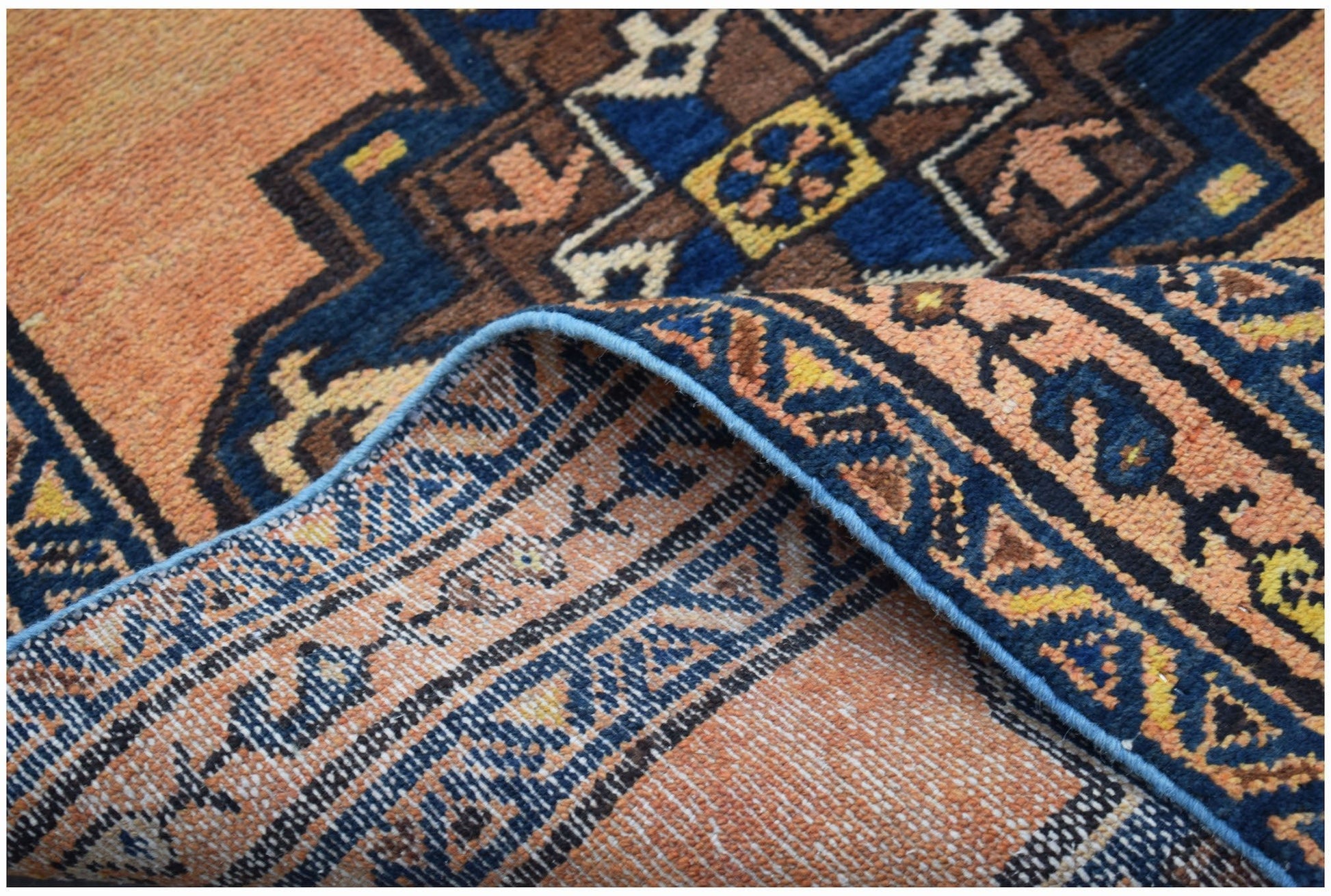 A handwoven vintage Persian rug featuring a geometric pattern in orange, blue, and brown tones.