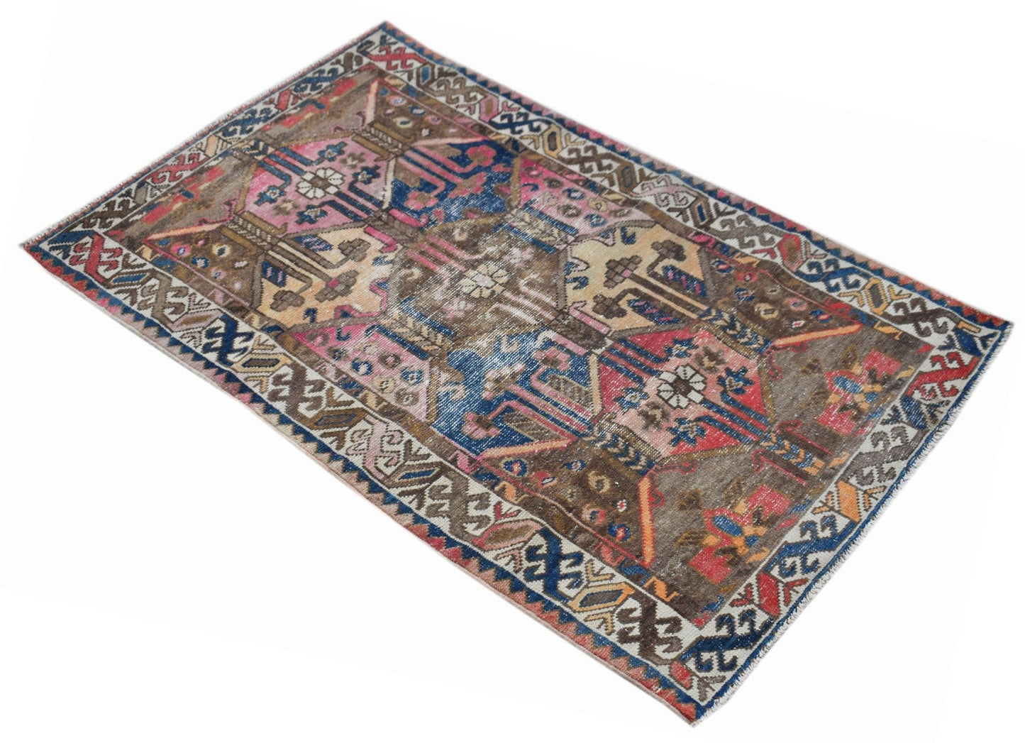 A vintage handwoven Persian rug featuring a distressed geometric pattern in blue, pink, and brown.
