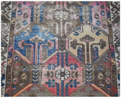 A vintage handwoven Persian rug featuring geometric floral patterns in blue, red, and brown tones.
