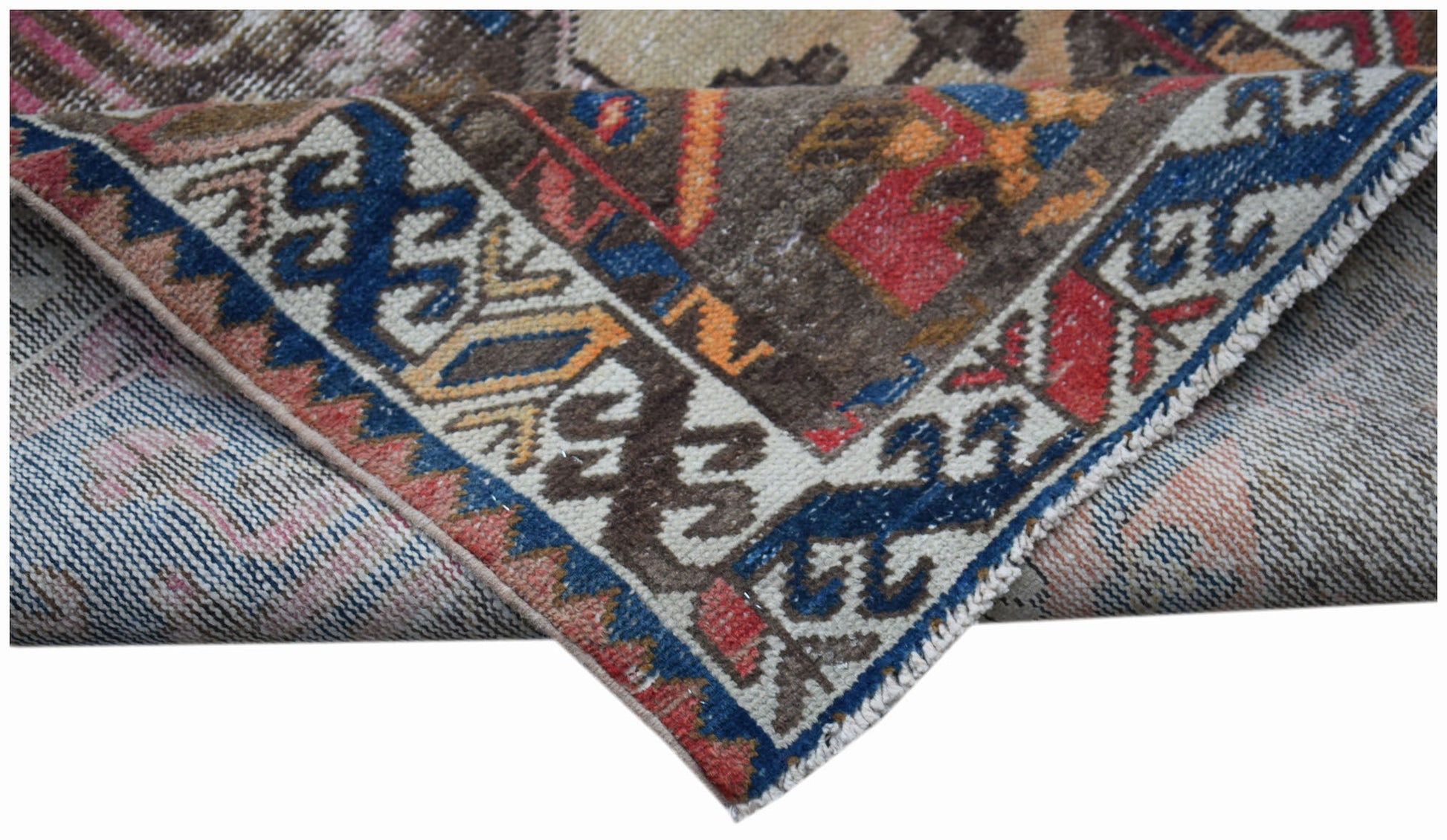 A folded vintage Persian rug featuring intricate geometric patterns in blue, red, and brown tones.
