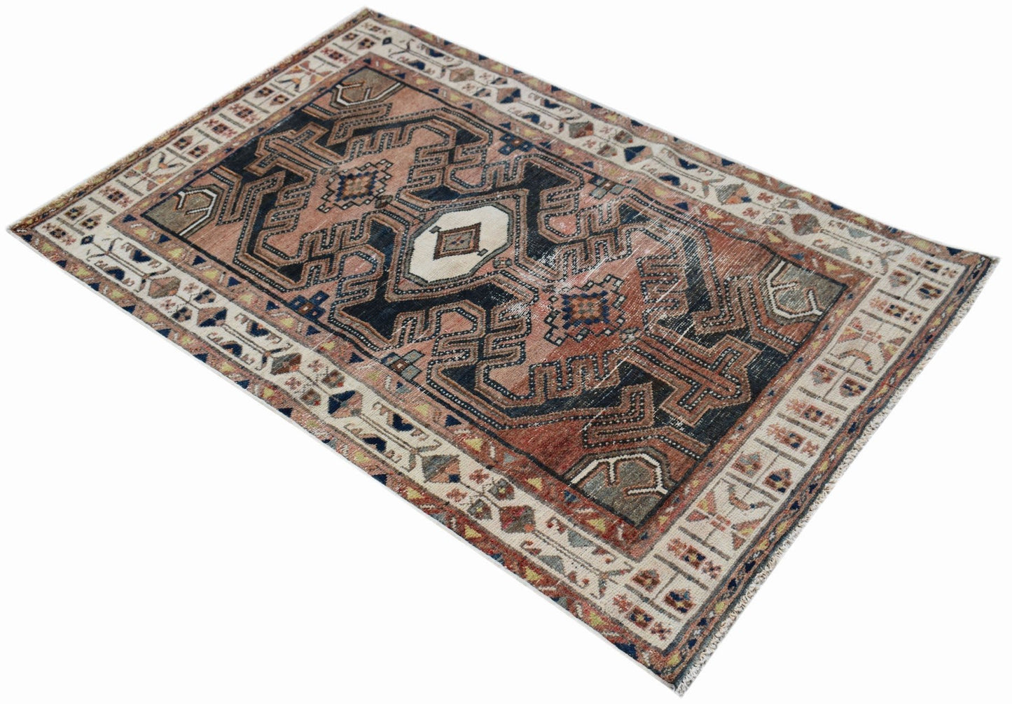 A handwoven vintage Persian rug featuring a geometric pattern in faded red, blue, and cream tones.