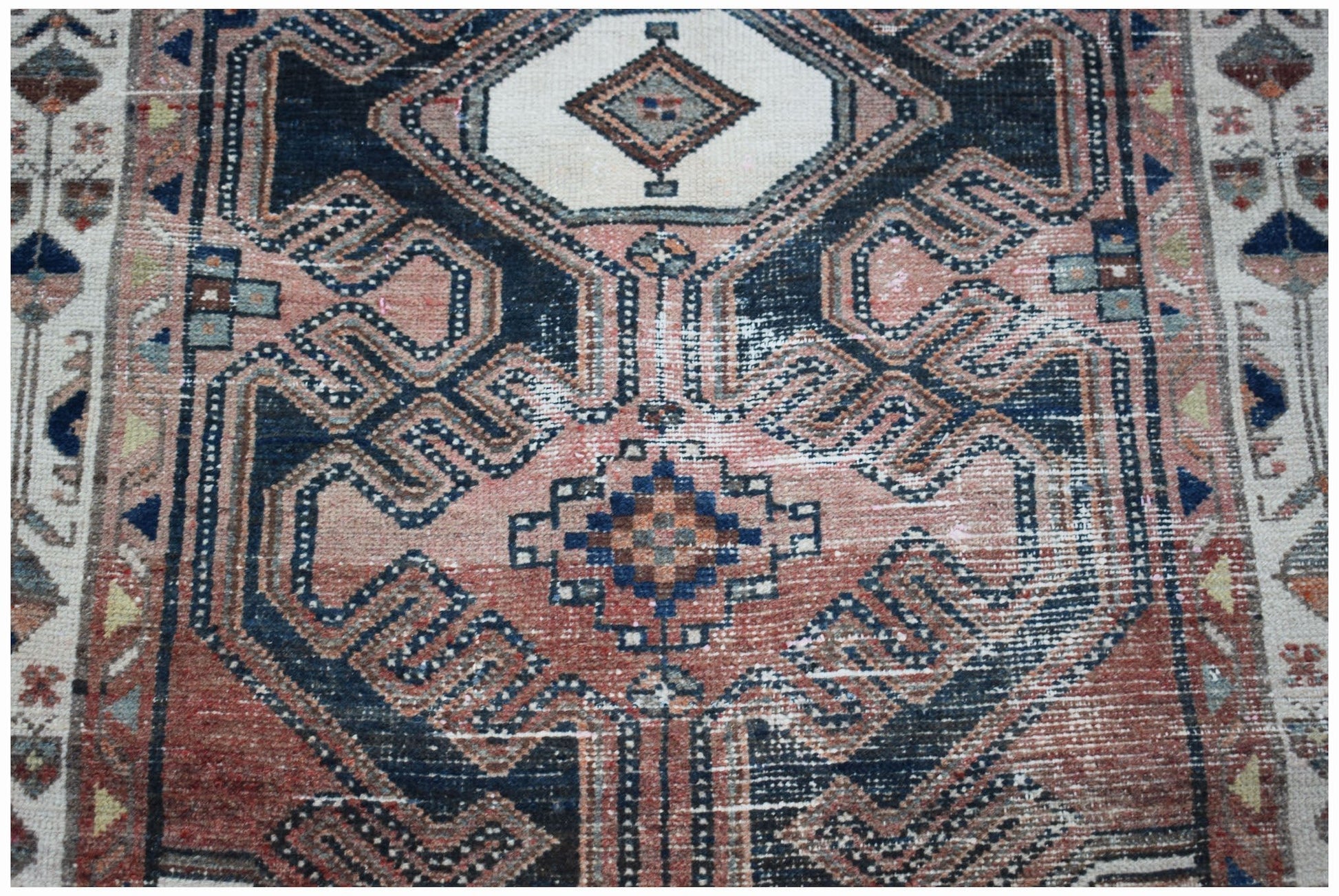 A vintage handwoven Persian rug featuring a geometric medallion pattern in faded red and navy blue.