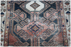 A vintage handwoven Persian rug featuring a geometric medallion pattern in faded red and navy blue.