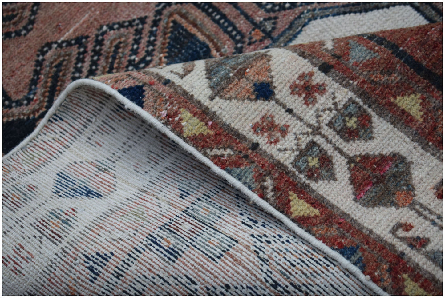 A corner of a handwoven vintage Persian rug showing its intricate patterned pile and cotton base.