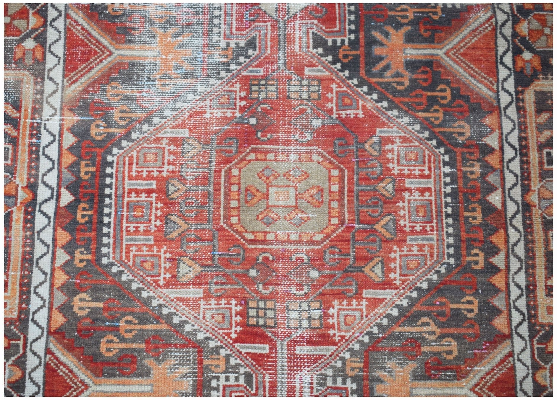 A vintage handwoven Persian rug featuring a geometric medallion pattern in red, grey, and orange.