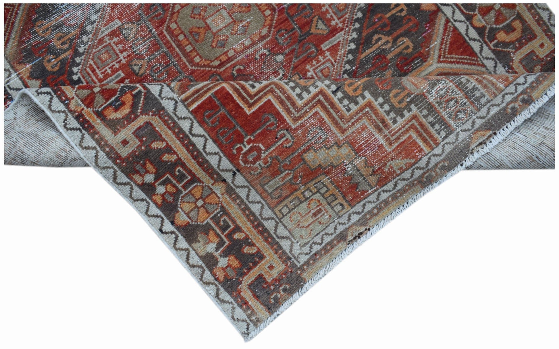 A handwoven vintage Persian rug featuring intricate geometric patterns in red, brown, and beige.